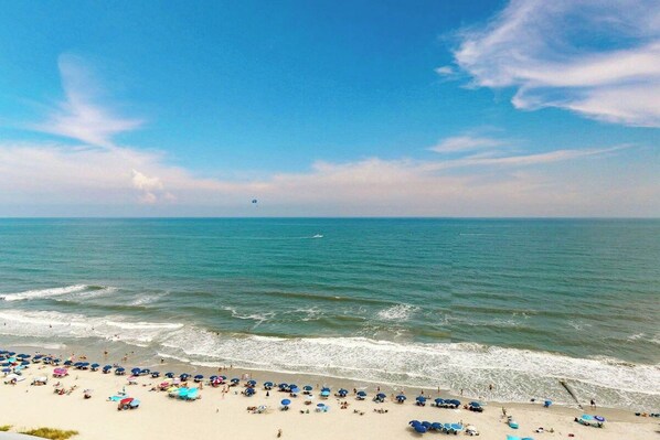 A beach with umbrellas and people, a clear sky, and the ocean.