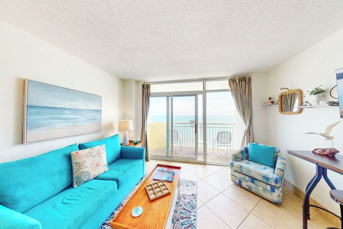 A living room with a sofa, a coffee table, and a view of the sea through a balcony door.