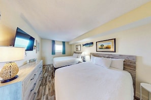 A hotel room with two beds, a desk with a lamp, and a television.