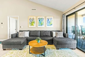 A living room with a sectional sofa, a round wooden coffee table, and three abstract paintings on the wall. - Coastal Comforts Retreat (Surfside Beach)