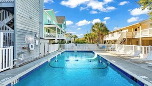 Una piscina con un indicador de profundidad de 3 pies, rodeada de edificios con balcones y una cerca blanca.