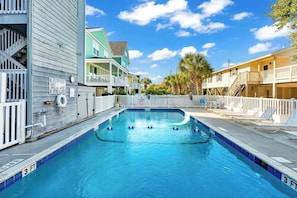 A swimming pool with a 3-foot depth marker, surrounded by buildings with balconies and a white fence. - Coastal Comforts Retreat (Surfside Beach)