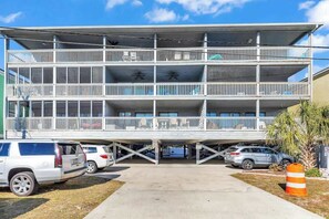 A multi-story building with balconies, parking spaces, and a clear sky. - Coastal Comforts Retreat (Surfside Beach)