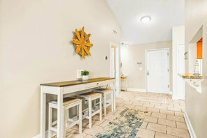 A hallway with a white desk, two stools, a decorative wall piece, and a patterned rug. - Coastal Comforts Retreat (Surfside Beach)
