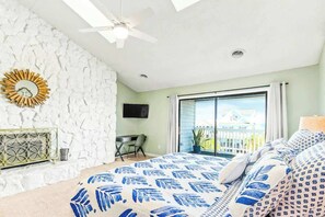 A bedroom with a large bed, a ceiling fan, a TV, a balcony with a view, and a stone wall. - Coastal Comforts Retreat (Surfside Beach)