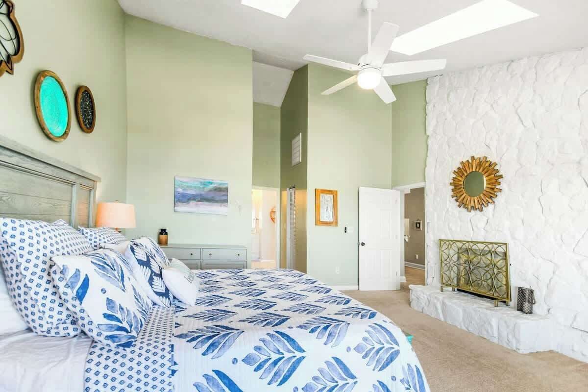 Une chambre à coucher comprenant un lit, un ventilateur de plafond, un mur blanc orné d’un motif texturé et une porte donnant sur une autre pièce.