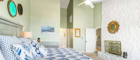 Une chambre à coucher comprenant un lit, un ventilateur de plafond, un mur blanc orné d’un motif texturé et une porte donnant sur une autre pièce.