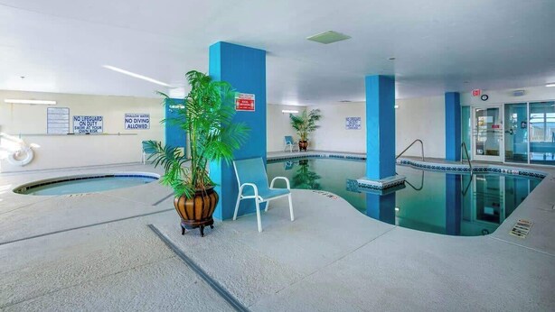 An indoor swimming pool with blue walls and a clear water surface. There are lounge chairs and a potted plant near the pool. - Bay Watch Resort 1637 (North Myrtle Beach)