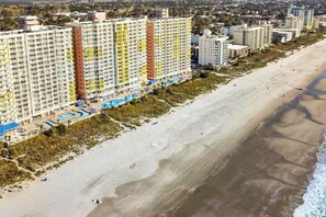 Ein Küstenhotel mit mehreren Hochhäusern, einer Strandpromenade und einem Poolkomplex.