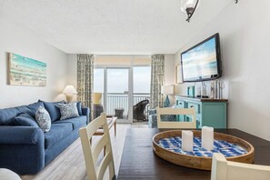 A living room with a sofa, a dining table with candles, a TV, and a view of the outdoors. - Bay Watch Resort 1635 Oceanfront (North Myrtle Beach)