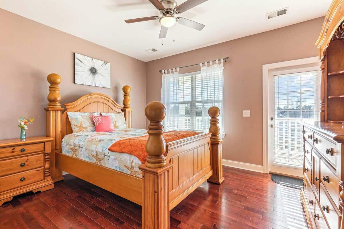 A bedroom with a wooden bed, a nightstand, a dresser, a ceiling fan, and a window with blinds.