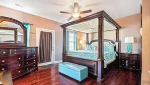 Uma cama de dossel com cortina, um espelho grande, um aparador de madeira e um banco em um quarto com piso de madeira.