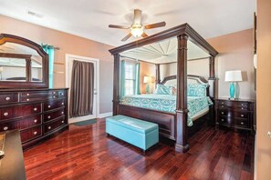 Ein Bett mit Himmelbett, ein großer Spiegel, eine Holzkommode und eine Bank in einem Zimmer mit Holzdielenboden.