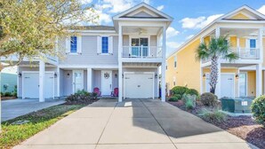 A row of two-story townhouses with attached garages, a central walkway, and a small garden area. - Tidewatch Charms Townhouse (North Myrtle Beach)