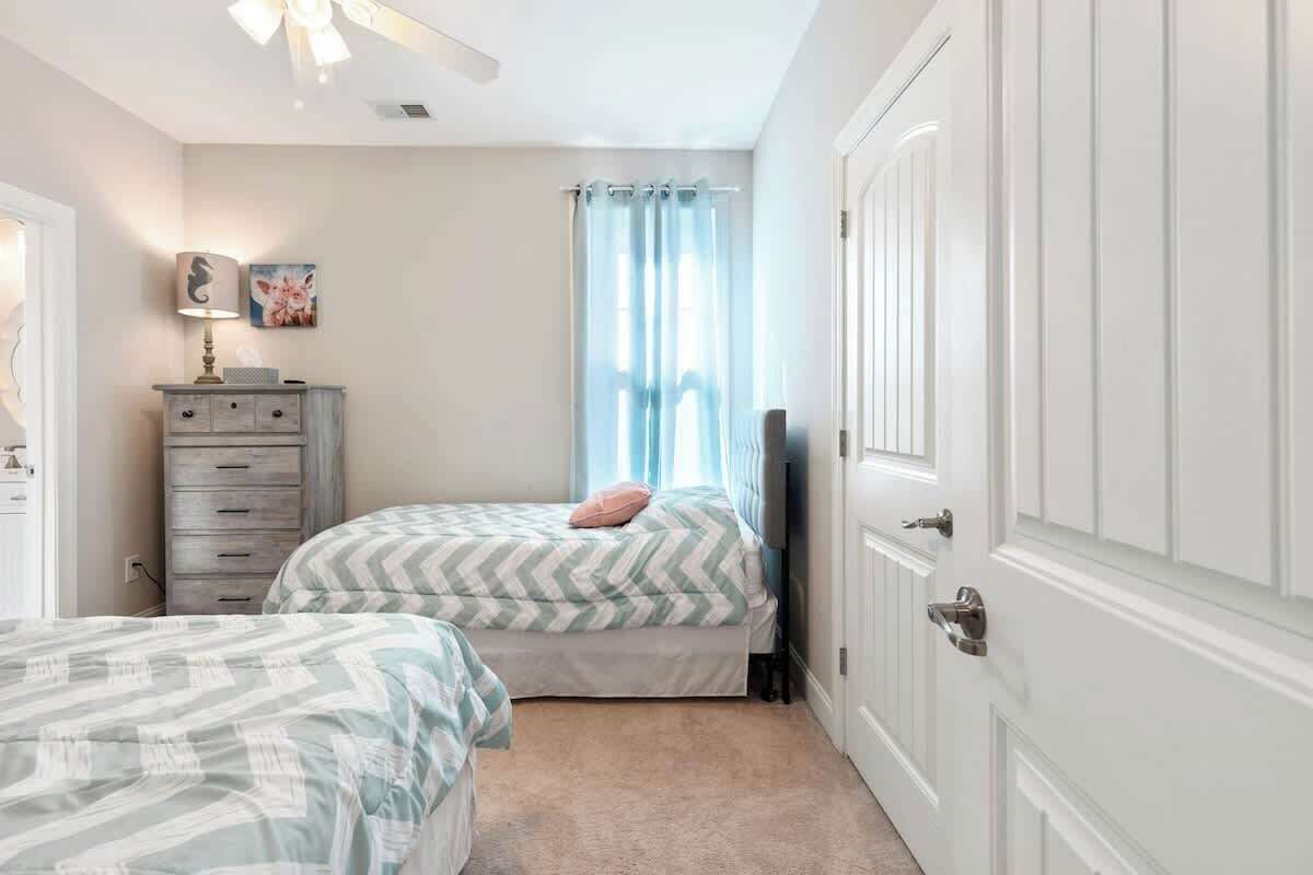 A bedroom with two beds, a dresser, a lamp, and a window with curtains.