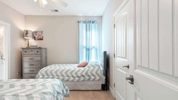 A bedroom with two beds, a dresser, a lamp, and a window with curtains. - Tidewatch Charms Townhouse (North Myrtle Beach)