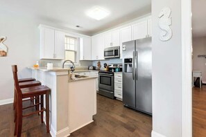 A modern kitchen with white cabinets, stainless steel appliances, and a wooden island with bar stools. - Tidewatch Charms Townhouse (North Myrtle Beach)