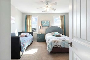 Une chambre avec deux lits, un ventilateur de plafond et une fenêtre avec des rideaux.
