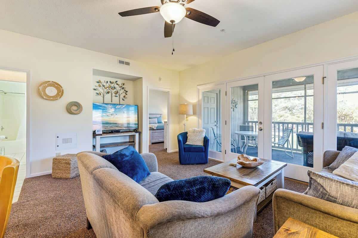A spacious living room with a ceiling fan, a television, and a view of the outdoors through large sliding glass doors.