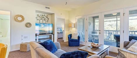 A spacious living room with a ceiling fan, a television, and a view of the outdoors through large sliding glass doors.