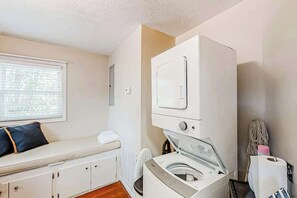 A compact laundry room with a washing machine, a drying machine, and a bench with a pillow. - GG's Place Beach House (Atlantic Beach)