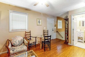 A room with a wooden floor, a round table with chairs, a sofa with patterned cushions, and a door leading to another room. - GG's Place Beach House (Atlantic Beach)