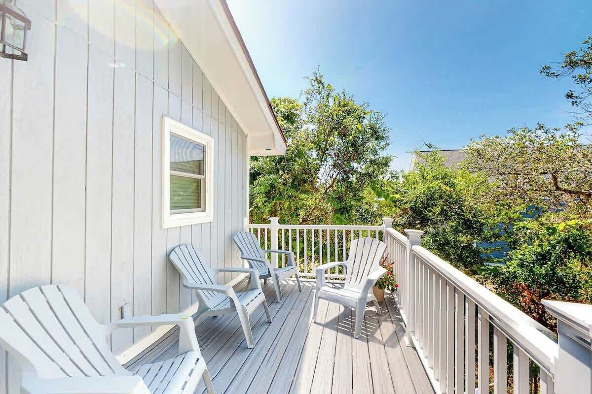 A wooden deck with white railings and several Adirondack chairs.