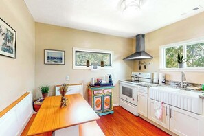 A kitchen with a wooden table, white cabinets, a stove, and a window with a view of trees. - GG's Place Beach House (Atlantic Beach)
