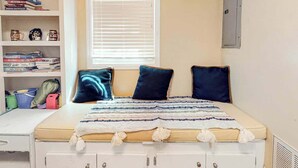 Ein Schlafzimmer mit Bett, Fenster mit Jalousien, einem Bücherregal und einem Schreibtisch.