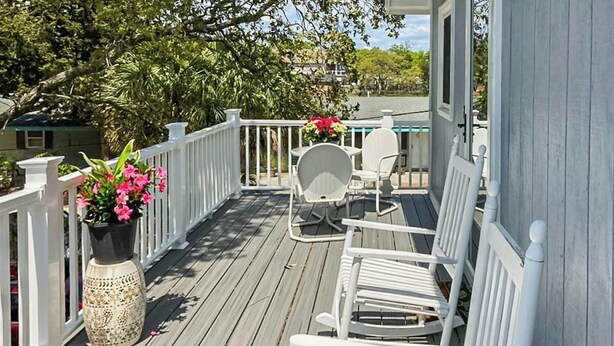 Eine Holzterrasse mit weißen Geländern, einem Tisch mit Stühlen und einem Blumentopf mit rosa Blüten.
