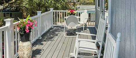 A wooden deck with white railings, a table with chairs, and a potted plant with pink flowers.