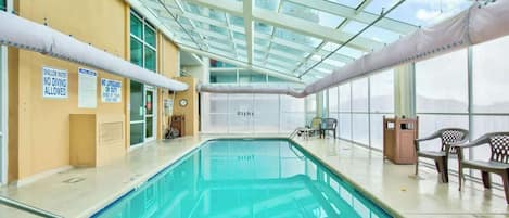 An indoor swimming pool with clear glass ceilings, safety signs, and seating areas.