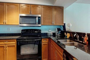 A kitchen with wooden cabinets, a stainless steel microwave, a black stove, and a sink. - Bahama Sands Unit 0508 (North Myrtle Beach)