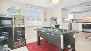 Een kamer met een tafelvoetbalspel, speelautomaten, een plafondventilator en een kitchenette.
