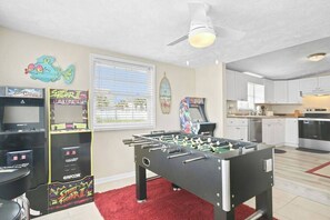 Ein Zimmer mit Kicker, Spielautomaten, Deckenventilator und einer Küchenzeile.