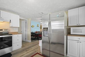 A compact kitchen with white cabinets, stainless steel appliances, and a microwave on the countertop. - Cherry on the Grove Condo (North Myrtle Beach)