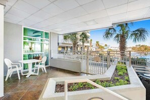 A balcony with a table and chairs, a railing, and a view of palm trees and a body of water. - Harbourgate 0526 - Serenity on The Marina (North Myrtle Beach)