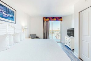 Habitación de hotel con una cama grande, televisión, cómoda y ventana con cortinas.