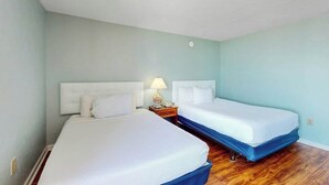 Ein Hotelzimmer mit zwei Betten, einem Nachttisch mit Lampe und Holzboden.