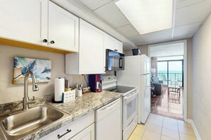 A modern kitchen with white cabinets, a granite countertop, stainless steel sink, and a built-in oven. - Ocean Park Resort 1222 (Myrtle Beach)