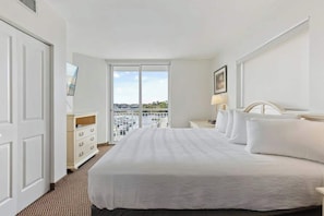 Ein Hotelzimmer mit einem großen Bett, einem Schreibtisch, einem Stuhl, einem Fenster mit Ausblick und einer Tür.