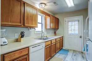 A kitchen with wooden cabinets, a dishwasher, a sink, and a window. - Blue Heron Beach Retreat (North Myrtle Beach)
