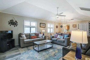 A living room with two sofas, a coffee table, a TV, and a ceiling fan. - Blue Heron Beach Retreat (North Myrtle Beach)