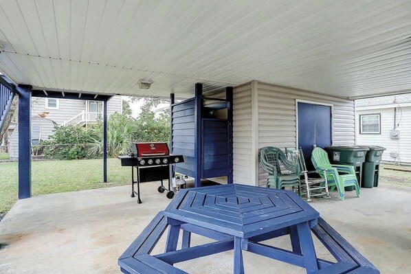 A covered patio area with a blue table and chairs, a barbecue grill, and green plastic chairs. - Blue Heron Beach Retreat (North Myrtle Beach)