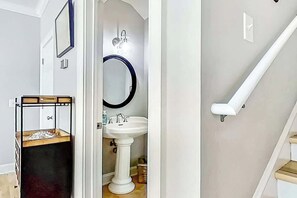 Un baño con lavamanos pedestal, un espejo de marco circular y un estante de madera con objetos.