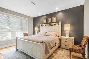 Un dormitorio con cama, mesitas de noche, una silla y una ventana con persianas.