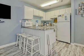 Una cocina con armarios blancos, encimera de mármol y una isla integrada con taburetes de bar.