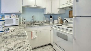 A kitchen with white cabinets, a microwave, a sink, and a stove. - PacMan Get Away Condo (North Myrtle Beach)