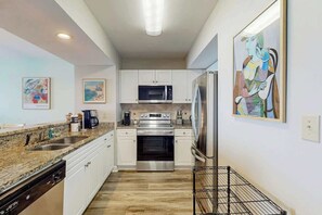 A modern kitchen with white cabinets, stainless steel appliances, granite countertops, and artwork on the walls. - Caribbean Resort and Villas 1107 (Myrtle Beach)