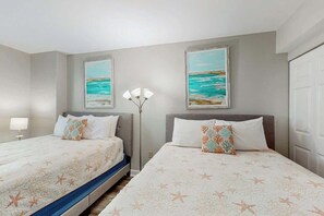 A hotel room with two beds, a nightstand, a lamp, and two framed paintings of the sea. - Caribbean Resort and Villas 1107 (Myrtle Beach)